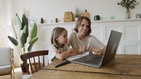 Ein-Hübsches-Blondes-Kleines-Mädchen-Liest-Die-Lektion-Auf-Dem-Laptopbildschirm,-Während-Sie-Ihr-Lächelnd-Zuhört