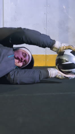 joven atleta se sumerge en el suelo para atrapar una pelota de fútbol que se mueve rápidamente en el lado izquierdo durante una sesión de entrenamiento intenso, mostrando agilidad y precisión atlética en un entorno deportivo bien iluminado