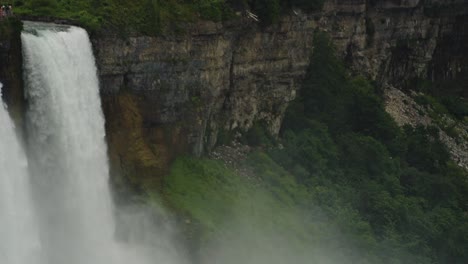 niagara falls plunges powerfully beside a weathered rock cliff layered in history and surrounded by lush greenery