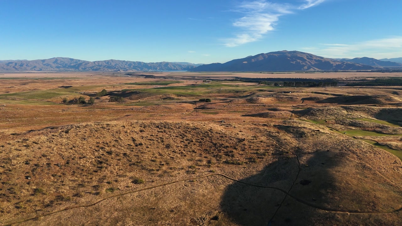 Flyover farmhouse on rolling golden mountain plateau, blue sky horizon