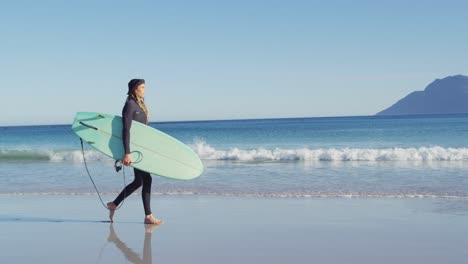 video of caucasian man with dreadlocks in wetsuit carrying surfboard walking on sunny beach