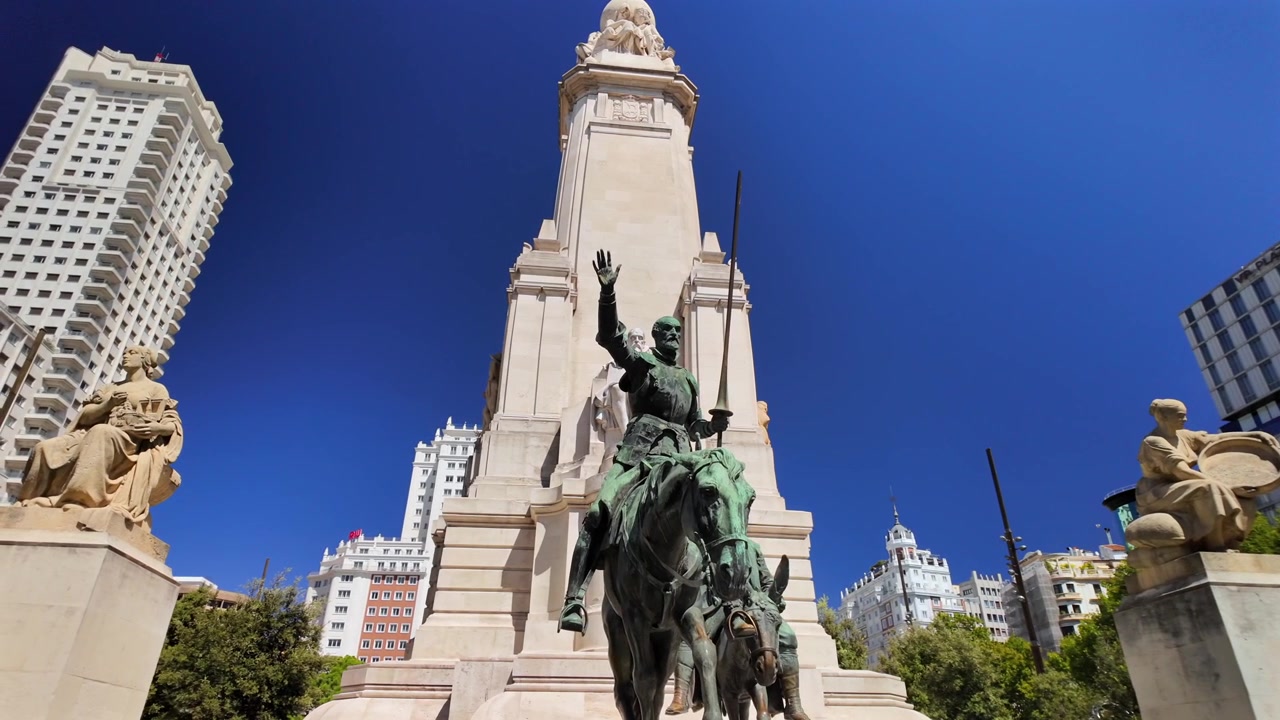 Vista ampla do Monumento a Cervantes e da estátua equestre de Dom Quixote rodeados por edifícios emblemáticos de Madrid