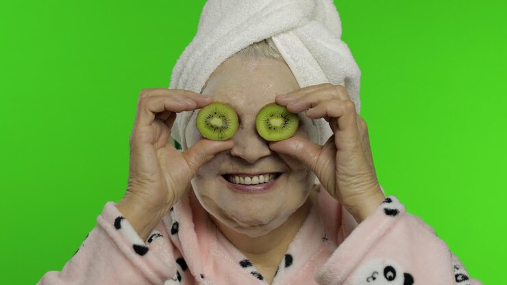 Elderly grandmother in bathrobe with bubble face mask. Old woman with kiwi