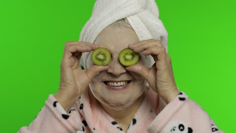 elderly grandmother in bathrobe with bubble face mask. old woman with kiwi