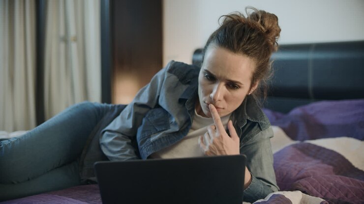 Junge Frau liegt mit Laptop auf der heimischen Couch