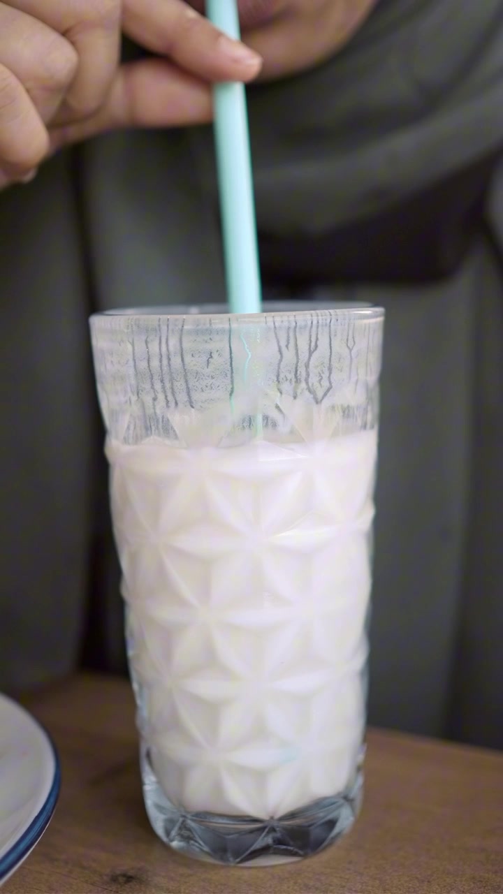 Primer plano de una mano removiendo leche en un vaso con una pajita