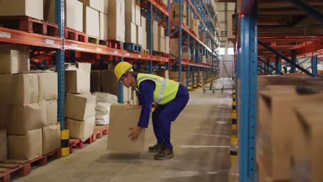 Asian-male-worker-wearing-safety-suit-with-helmet-and-carrying-boxes-in-warehouse