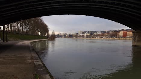 Vista-Del-Puente-De-Hierro:-Un-Vistazo-Debajo,-El-Paseo-Junto-Al-Río-De-Lyon-Adornado-Con-Un-Velo-Invernal-Que-Invita-A-La-Tranquilidad