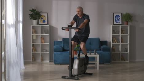 Un-Hombre-Tranquilo-Y-Deportivo-De-Mediana-Edad-Está-Entrenando-En-Una-Bicicleta-Giratoria-En-La-Sala-De-Estar,-Fitness-En-Casa-Y-Un-Estilo-De-Vida-Saludable-Para-Mantenerse-En-Forma