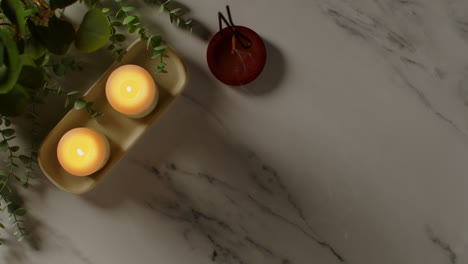 overhead view looking down on still life of lit candles with green plants and person picking up towels as part of relaxing spa day decor