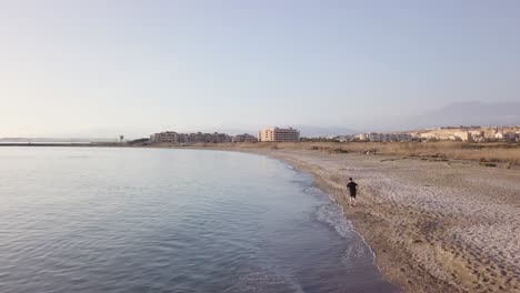 young runner man training on beautiful sunset at beach. drone view
