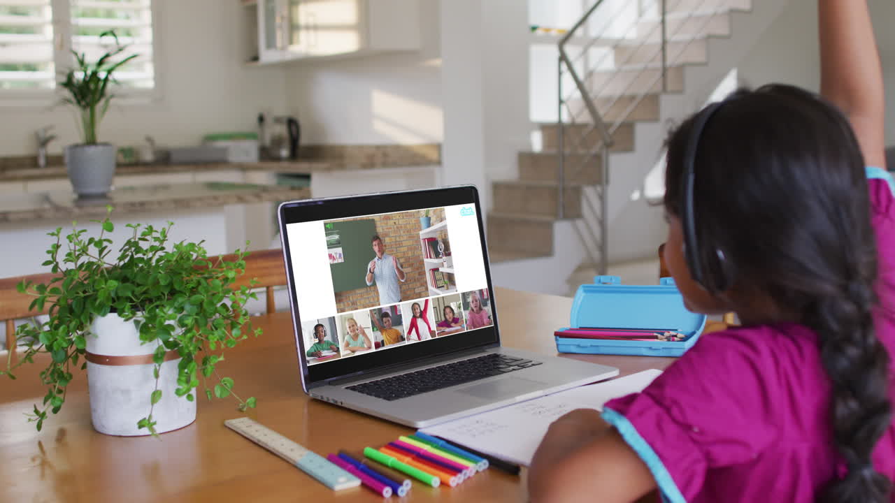 Schoolgirl using laptop for online lesson at home, with diverse teacher and class on screen