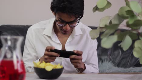 young man playing games on his phone while snacking on crisps