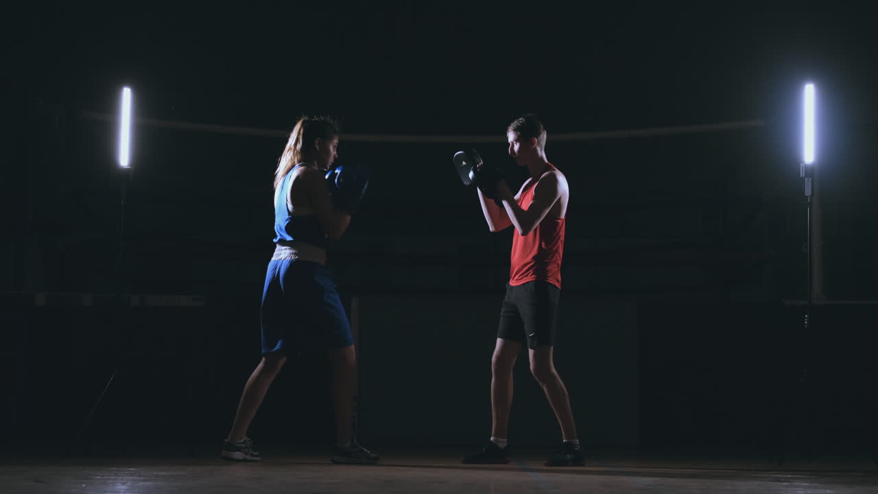Female boxer punching a focus mitts with boxing gloves in a smoky gym