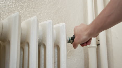 ajuste de la temperatura del radiador de hierro a mano girando la válvula en una habitación luminosa