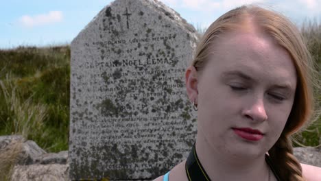 young redheaded girl stairs at camera with large old tombstone in the background