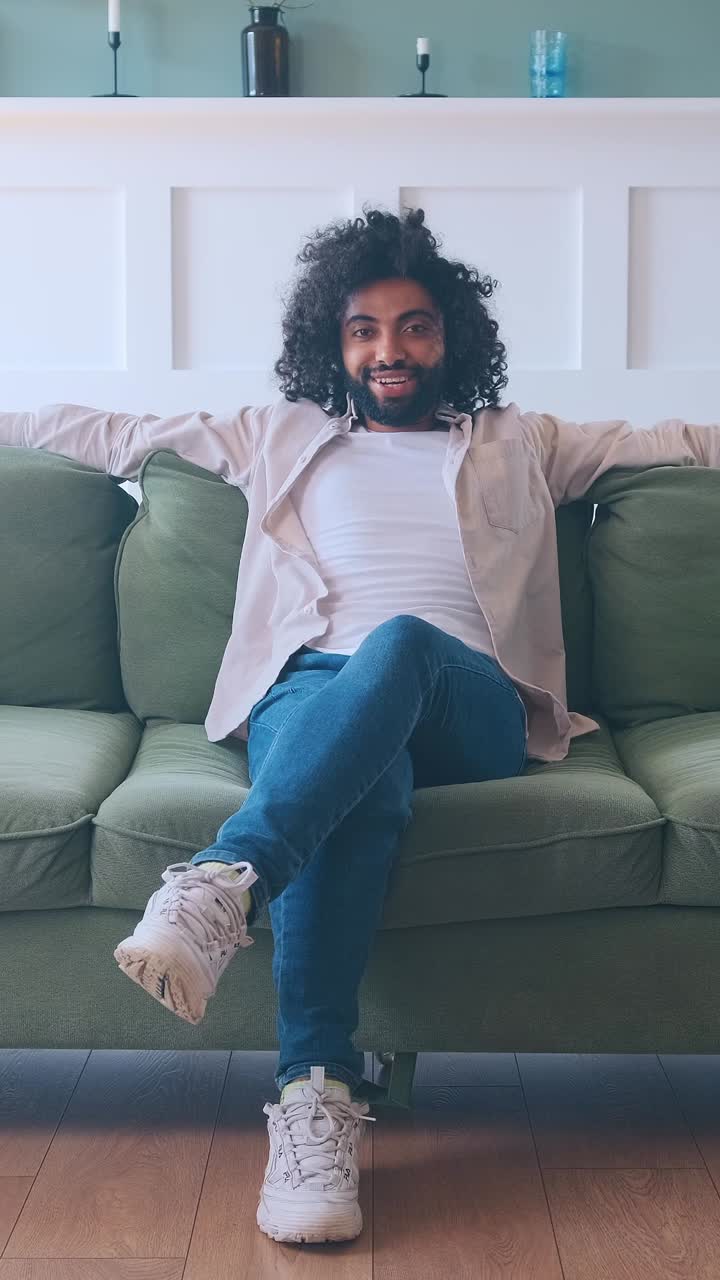 Young smiling successful arabian man sits on sofa with arms at sides