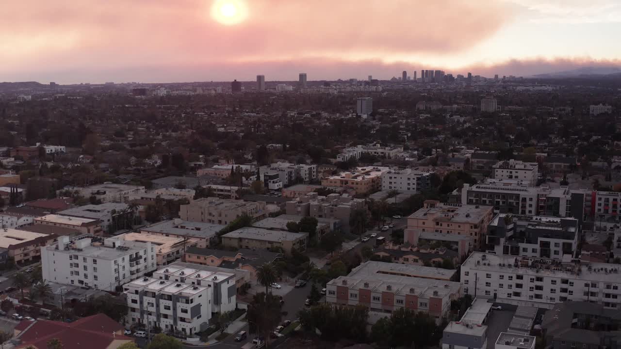 Low aerial shot flying over Melrose Hill with smoke from the Palisades Fire in the horizon at sunset in Hollywood, California. 4K