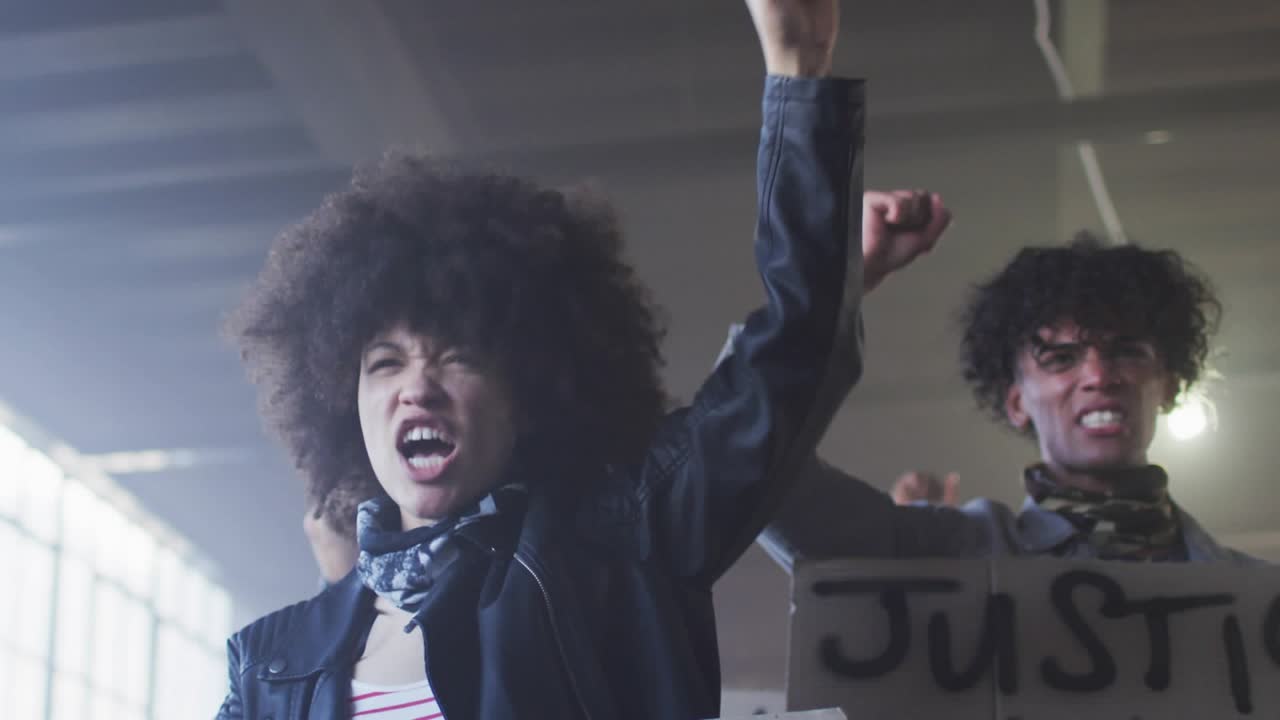 Woman and man raising fists and shouting in warehouse sparking animated icons covering protest sign