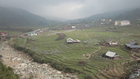 river flowing through terraced rice fields and scattered houses in sa pa, vietnam, on a cloudy day