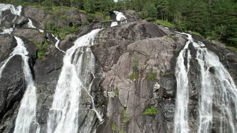 long aerial dolly shot pulling out from the top of laukelandsfossen waterfall in norway, revealing a wide waterfall with many streams of water cascading over the rocky cliff face