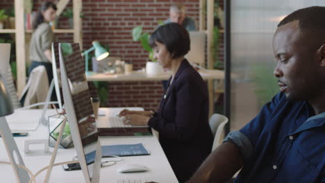 Joven-Hombre-De-Negocios-Afroamericano-Escribiendo-Una-Lluvia-De-Ideas-Usando-Una-Computadora-Trabajando-En-Un-Espacio-De-Trabajo-De-Oficina-Multiétnico-Creativo-Compañeros-De-Trabajo-Colaborando-Con-Un-Fondo-Ocupado