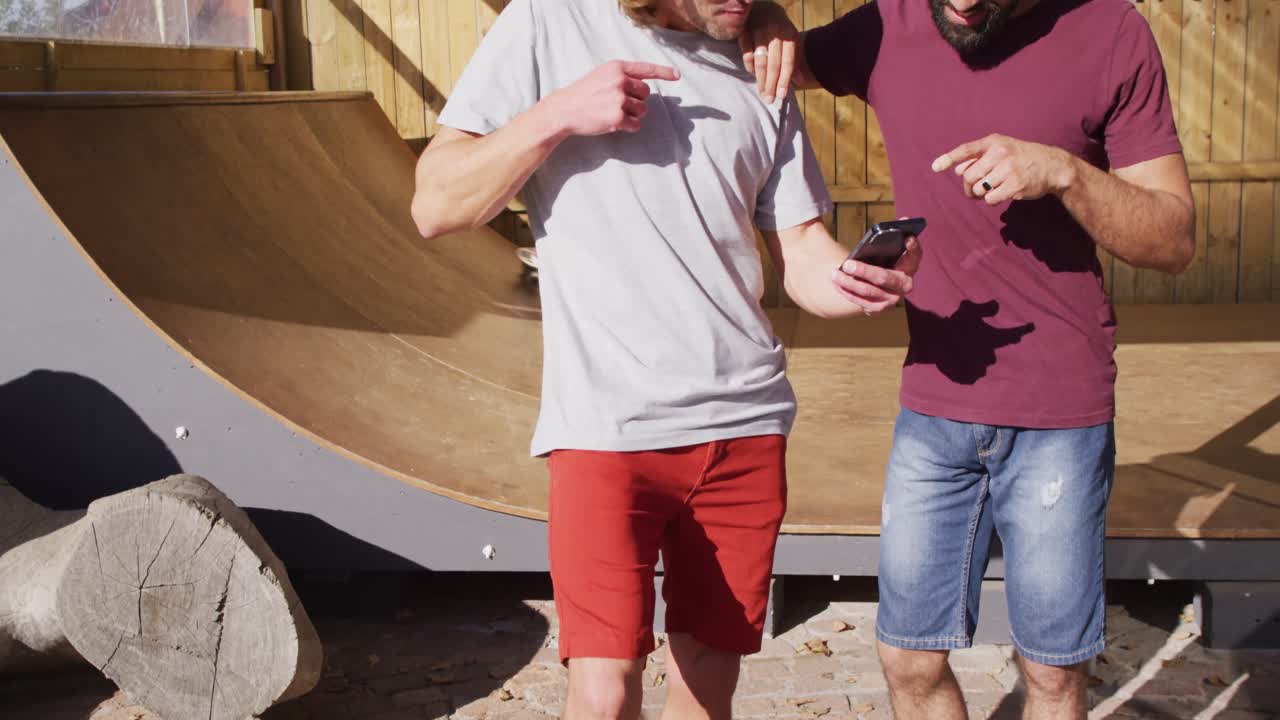 video de hombres felices y diversos patinadores usando teléfonos inteligentes en el parque de patinaje