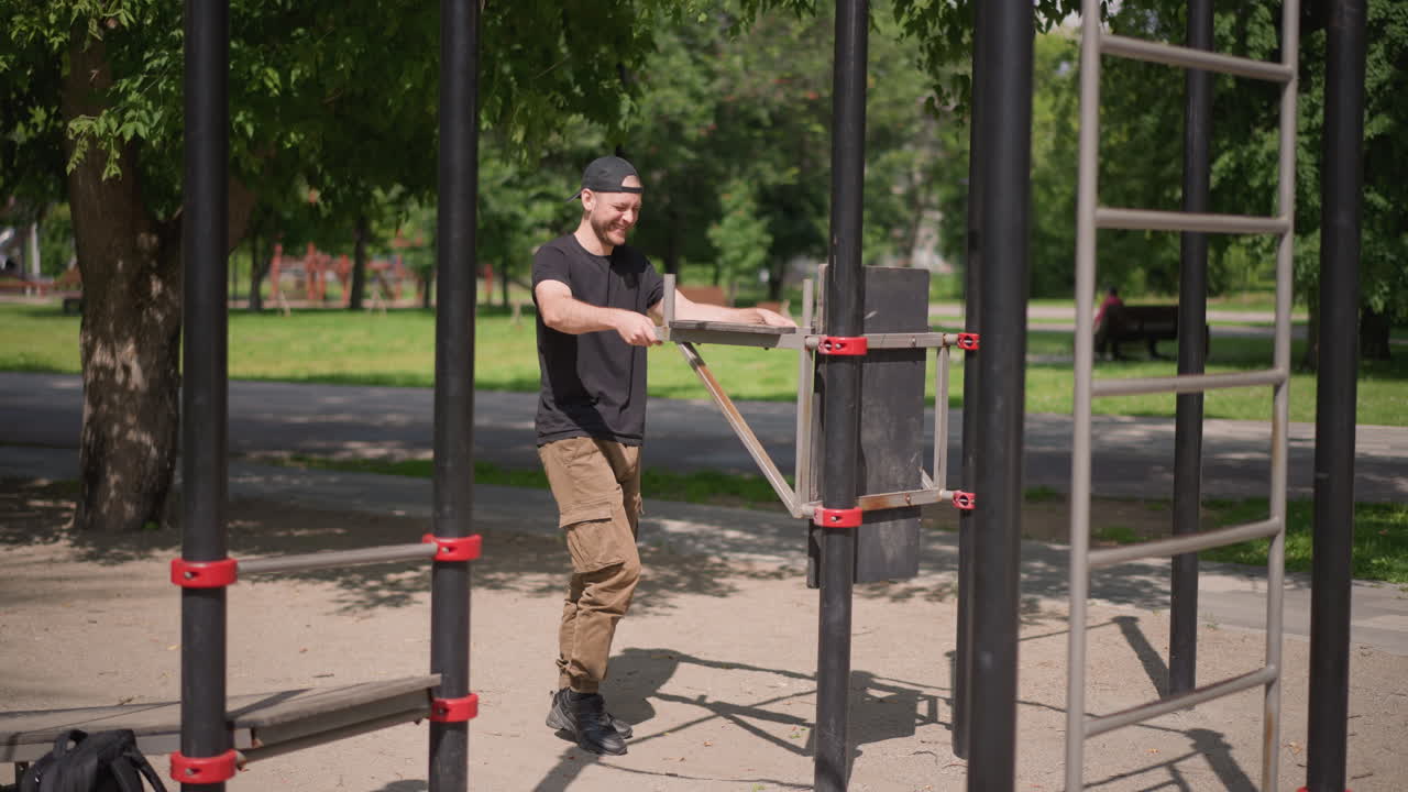 White Man Training On Outdoor Bars, Steady Rhythm And Focused Posture As He Navigates Metal Ladder And Parallel Bars, Summer Park Backdrop, Casual Athletic Clothing And Cap, Deliberate Grip