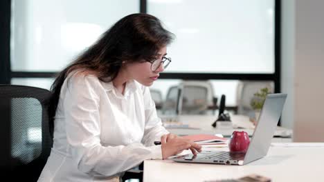 una mujer de negocios enfocada y hermosa trabajando en una computadora portátil sentada en una oficina corporativa.