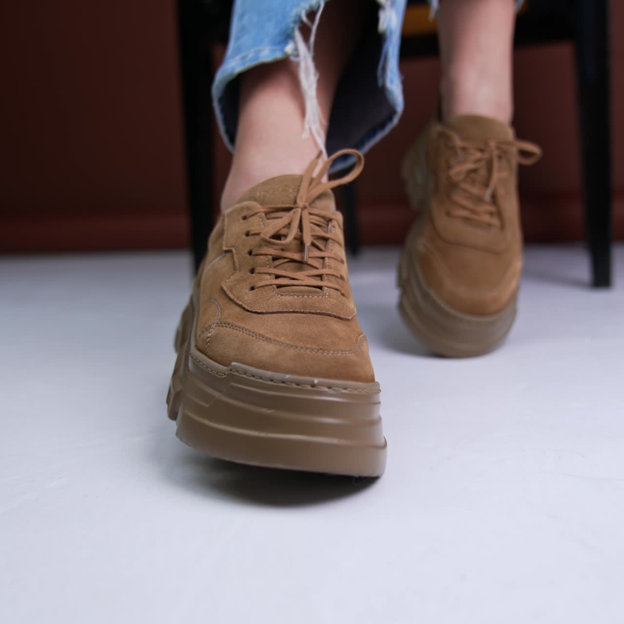 Brown suede shoes on the tractor soles. Lady in jeans sitting on the chair posing in her stylish modern footwear in front of camera