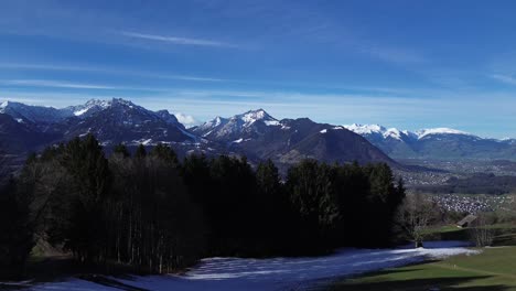 drone rise up in sky fly above forest and reveal amazing winter mountain landscape with snowcapped mountains on a sunny day in vorarlberg austria