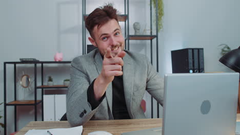 Businessman-working-on-office-laptop-pointing-to-camera-looking-with-happy-expression-making-choice