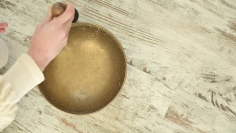 Crop-sound-therapist-playing-bowl-gong-with-rippled-aqua