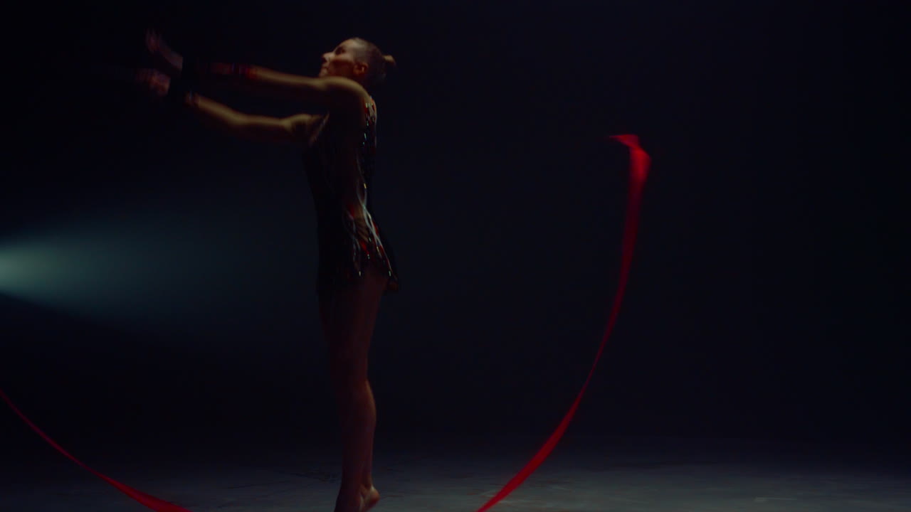 donna flessibile che salta con un nastro di ginnastica. giovane ginnasta che si esibisce all'interno.