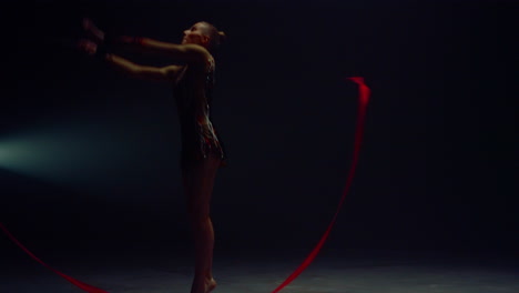 flexible woman jumping with gymnastic ribbon. young gymnast performing indoors.