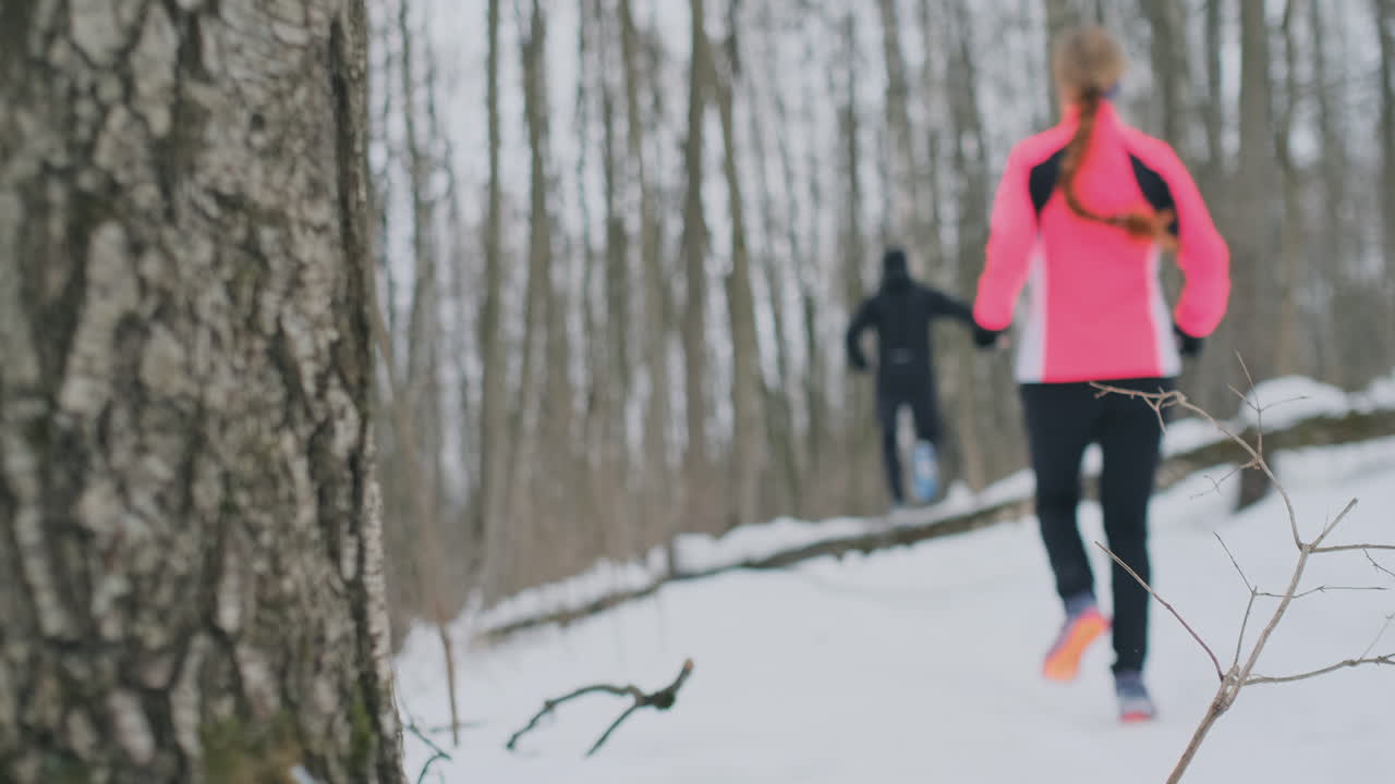 Positive beautiful young healthy couple running with sportswear through the forest in the sunny winter morning. Jump over the tree, overcome the difficulties of the path. step over an obstacle