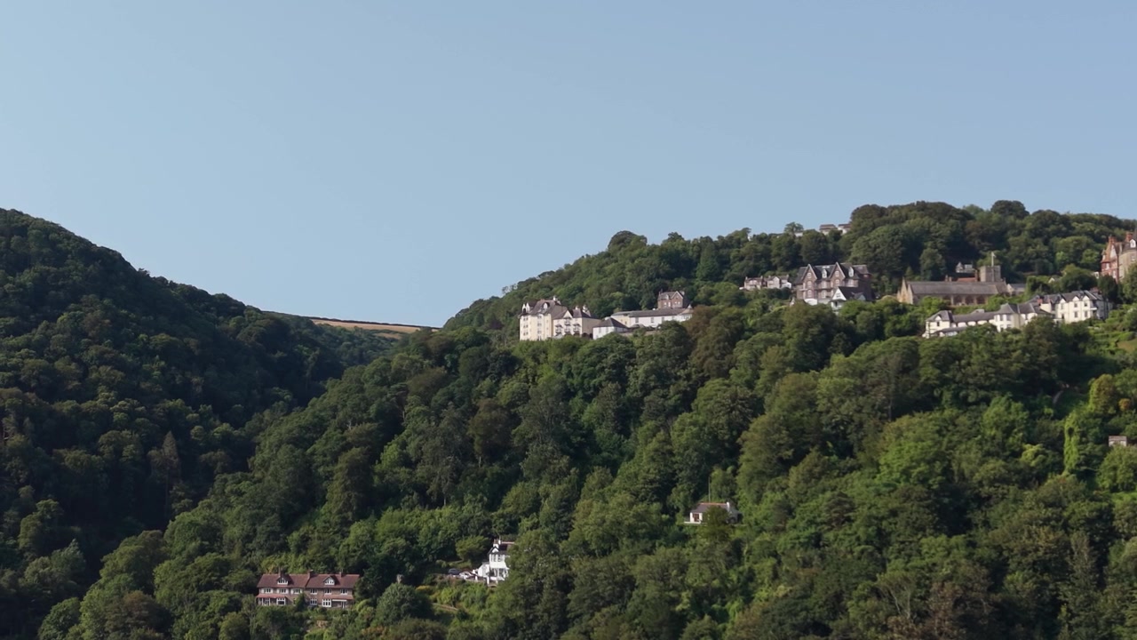Paesaggio costiero con scogliere boscose e case annidate tra gli alberi vicino a Lynmouth nel North Devon, Regno Unito