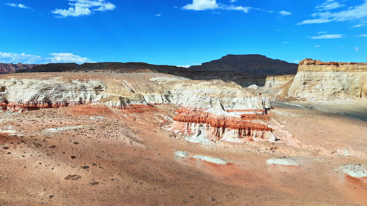 Flying over the barren desert lit by the bright hot sun. Approaching bare rocks under blue sky with little white clouds. Arizona, USA