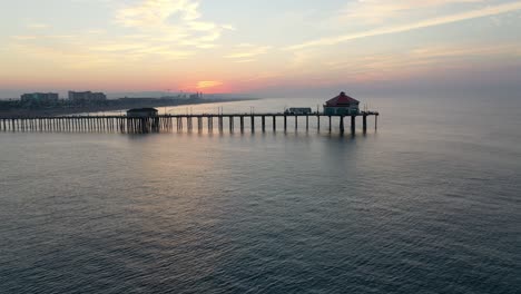 Eine-Atemberaubende-4k-Parallaxansicht-Von-Wunderschönen-Luxushotels-Am-Strand,-Wie-Sie-Bei-Sonnenaufgang-Durch-Den-Pier-In-Der-Sonnigen-Südkalifornischen-Surfstadt-USA-Zu-Sehen-Sind