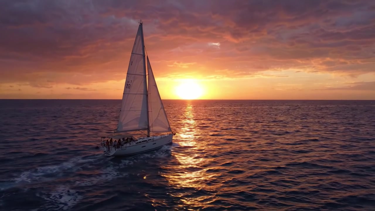 Un impresionante viaje en velero al atardecer: experimente la tranquilidad de una embarcación deslizándose contra un horizonte dorado y cielos nublados vibrantes.