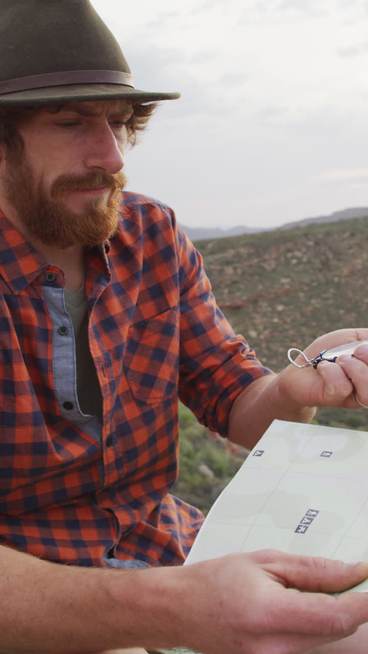 video vertical de un sobreviviente caucásico barbudo con mapa y brújula explorando el desierto
