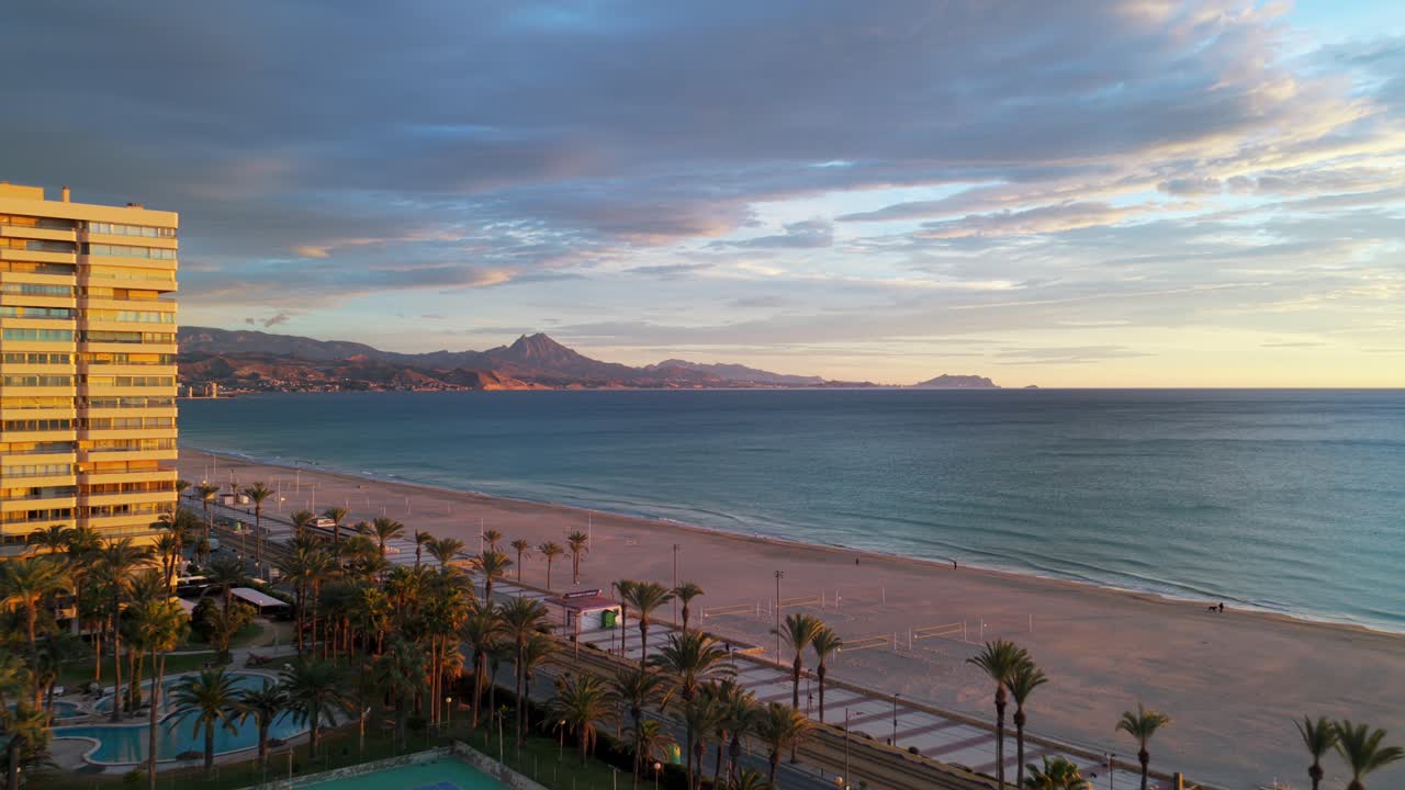Scena costiera con condominio, spiaggia, palme e mare Mediterraneo al tramonto