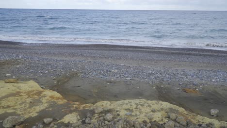 View-of-waves-lapping-on-the-beach,-covered-in-extractive-waste