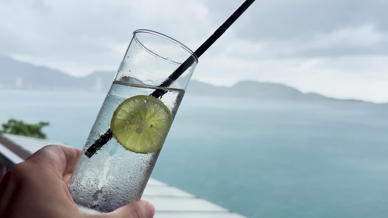 A hand holds a lime soda against a scenic ocean backdrop in Phuket, Thailand, capturing a serene and refreshing moment