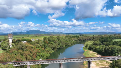 Vista-Aérea-De-La-Línea-Ferroviaria-Mirani-Y-El-Puente-De-La-Carretera-Mackay-Eungella,-Que-Muestra-El-área-De-Picnic-De-La-Playa-Platypus-Y-Un-Denso-Y-Exuberante-Bosque-En-Las-Orillas-Del-Río-Pioneer