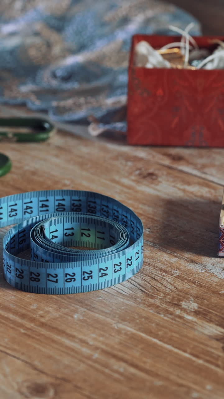 Seamstress is taking blue tape measure from the wooden table in atelier. Fingers of young female designer are taking the band with centimeter among sewing accessories. Vertical video