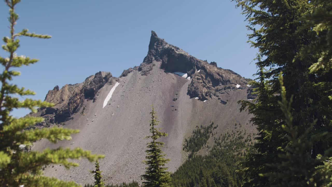 Montagna appuntita con alberi in primo piano.