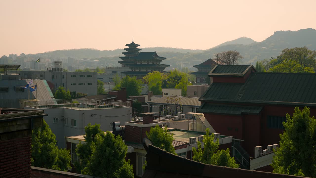 Gyeongbokgung Palace’s multi-tiered pagoda rises above modern rooftops with mountain views in Jongno-gu, Seoul. Wide shot