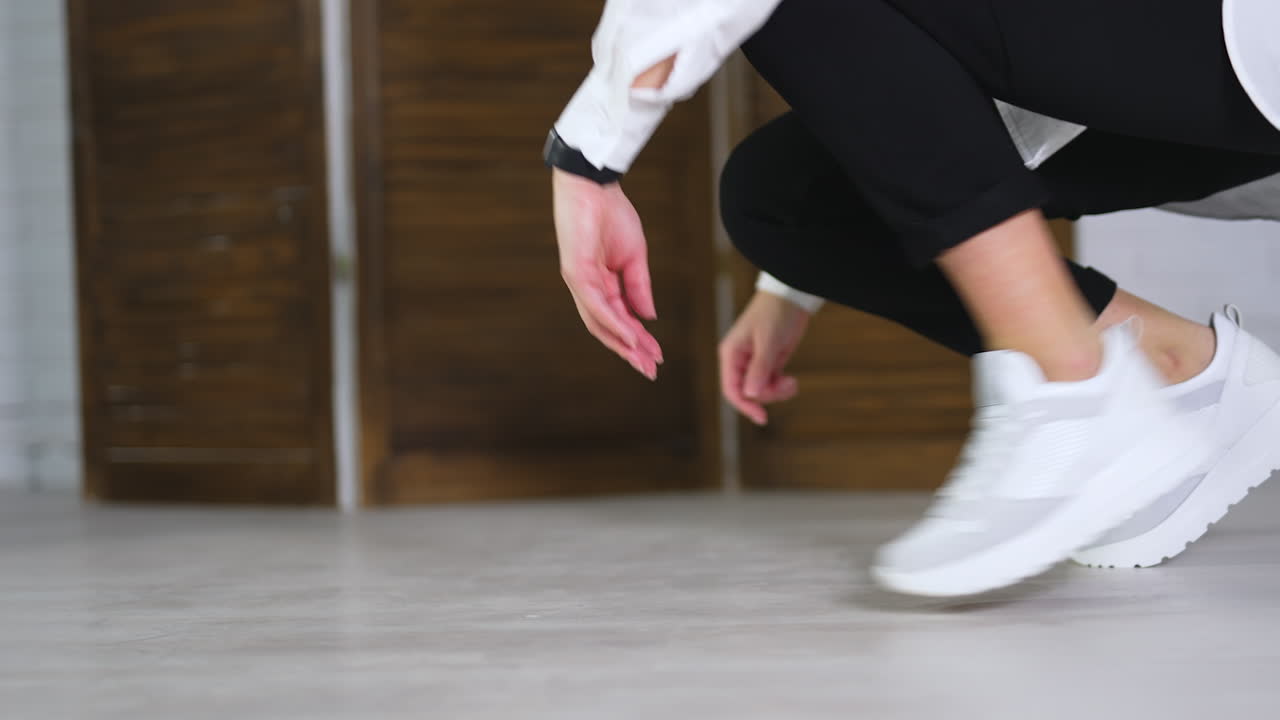 Lady demonstrates white sport footwear. Woman squatted to touch up comfortable sneakers. Close up. Blurred backdrop.