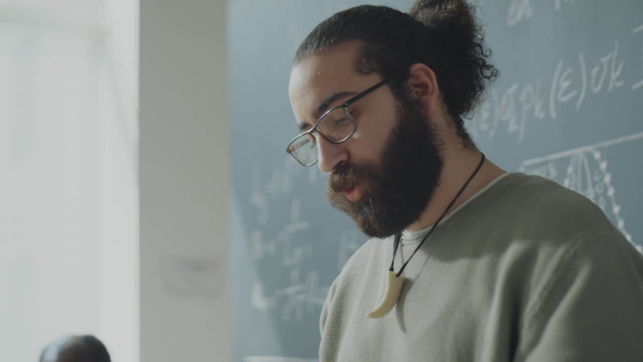 A bearded man with glasses in front of a chalkboard filled with mathematical equations
